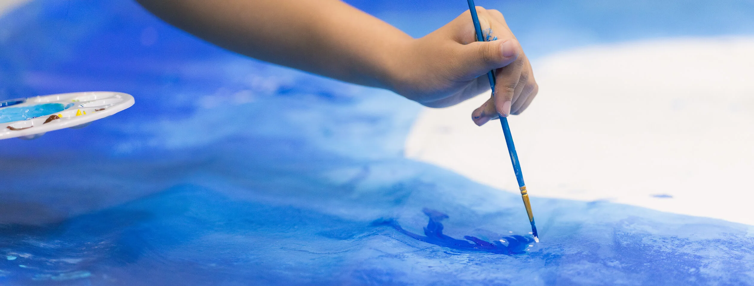 A child’s hand painting a canvas in blue